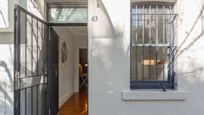 Ein weißes Gebäude mit schwarzem Tor, einem vergitterten Fenster und der Nummer 63 an der Wand.