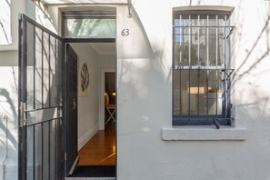 Ein weißes Gebäude mit schwarzem Tor, einem vergitterten Fenster und der Nummer 63 an der Wand.