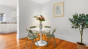Ein Essbereich mit einem runden Tisch, vier Stühlen, einer Blumenvase, einem gerahmten Bild an der Wand und einer Topfpflanze.
