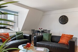 A modern living room with a black leather sofa, a glass coffee table, and a dining area with a black clock on the wall. - West Bridgford Luxury 2 bed 2 Bath Apartment (Nottingham)