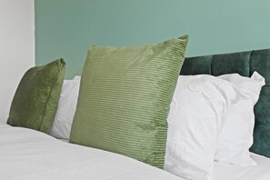 A bed with white bedding and three pillows, two green and one white, against a teal wall. - West Bridgford Luxury 2 bed 2 Bath Apartment (Nottingham)