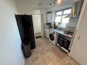 A compact kitchen with a washing machine, a stove, and a trash bin. - Ultra-Spacious 2 BR In Central Wimbledon! (Greater London)