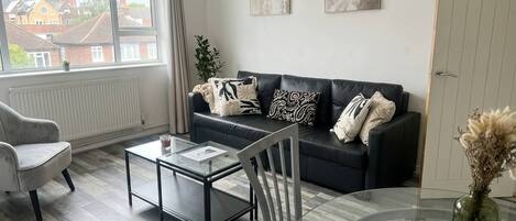 A modern living room with a sofa, armchairs, a glass coffee table, and a view of the outside.