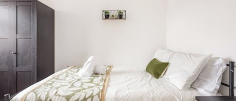 A neatly made bed with a white and green patterned blanket, a green pillow, and a small shelf with plants on the wall.