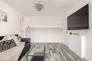 Un saló modern amb una taula de centre de vidre, un sofà de cuir negre i un televisor de pantalla plana gran fixat a la paret.