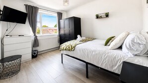 A modern bedroom with a bed, a TV, a wardrobe, and a window with curtains. - Ultra-Spacious 2 BR In Central Wimbledon! (Greater London)