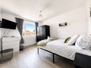 Ein modernes Schlafzimmer mit Bett, Fernseher, Kleiderschrank und einem Fenster mit Vorhängen.