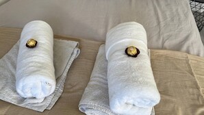 A bed with two neatly folded white towels, each with a gold nut on the center.