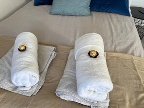 Een bed met twee keurig gevouwen witte handdoeken, elk met een gouden noot in het midden.