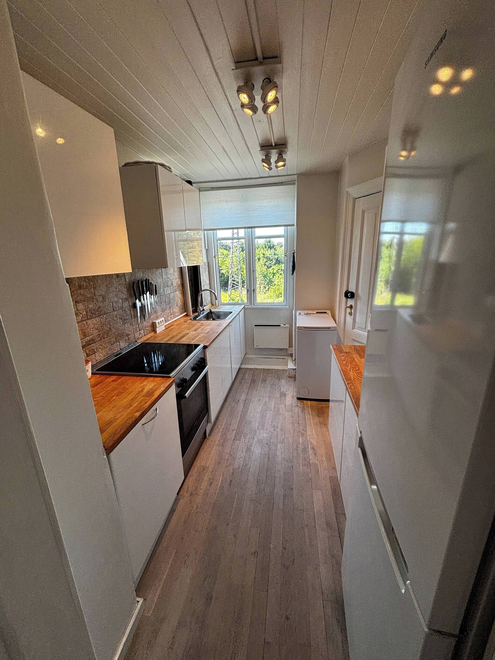 A modern kitchen with a wooden countertop, stainless steel appliances, and a view through a window.