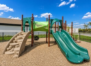 Ein Spielplatz mit Rutsche, Kletterstufen und einer grünen Kletterkonstruktion.
