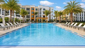 Ein Pool mit Liegestühlen und Palmen, umgeben von mehrstöckigen Gebäuden mit Balkonen.