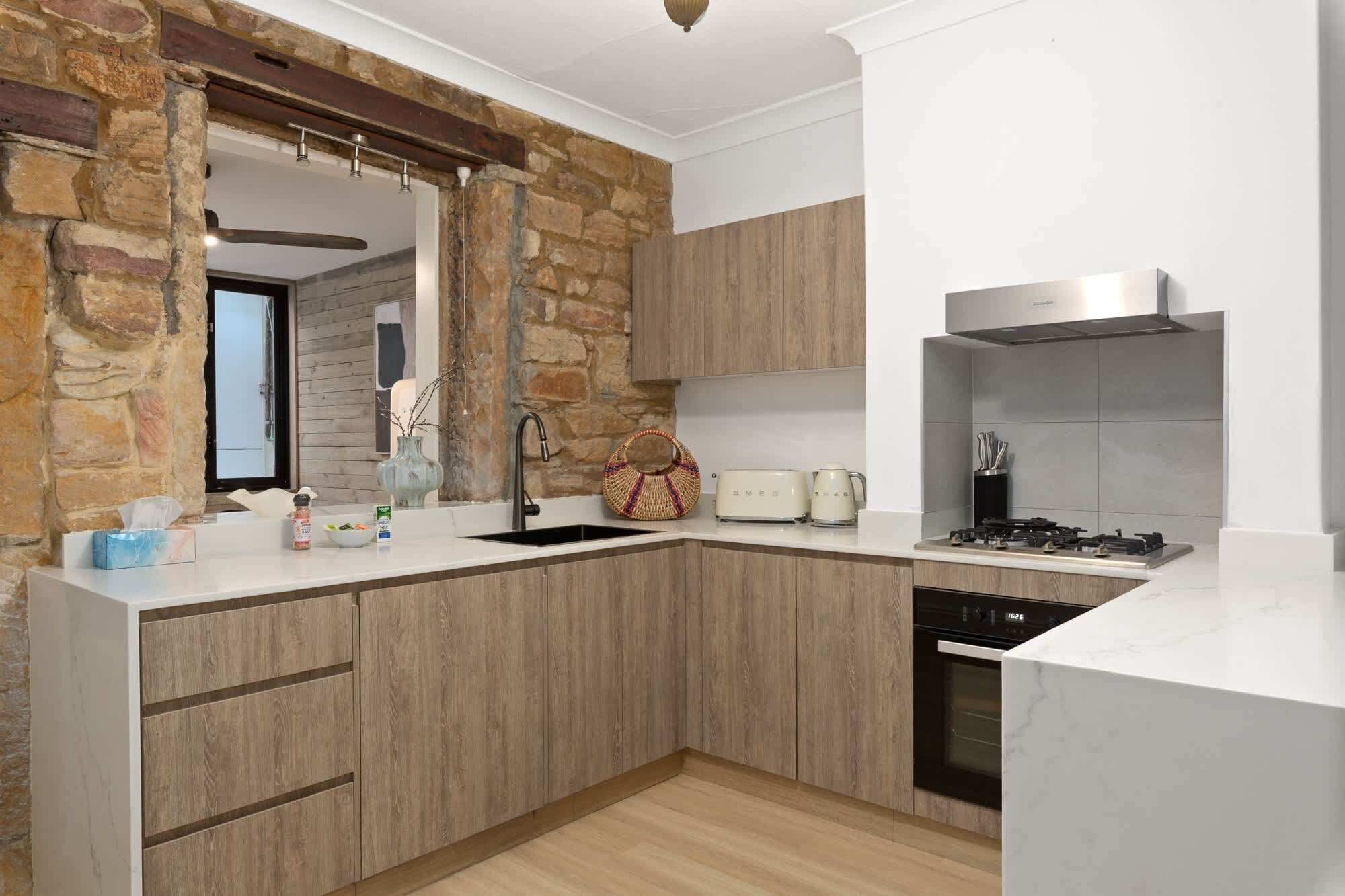 A modern kitchen with a stone accent wall, wooden cabinets, a built-in oven, and a gas stove.