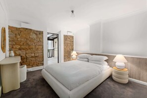 Ein modernes Schlafzimmer mit einer Wand aus Stein, einem großen Bett mit weißer Bettwäsche, zwei Nachttischlampen und einem kleinen Nachttisch.