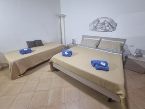 A hotel room with two single beds, each with a beige bedspread and blue towels. There is a wall-mounted artwork above the beds and a bedside table with a lamp and a decorative item. - Charming Villa Rental in Mazara Del Vallo with Pool Access (Mazara Del Vallo)
