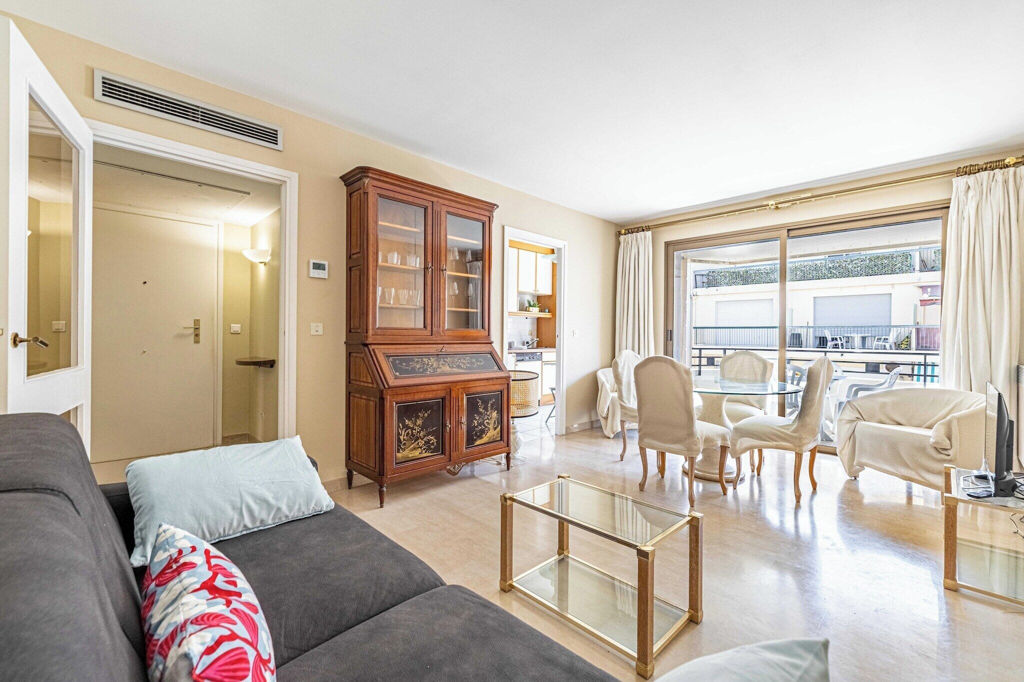 A living room with a sofa, chairs, a glass coffee table, a cabinet, and a view of the outside.
