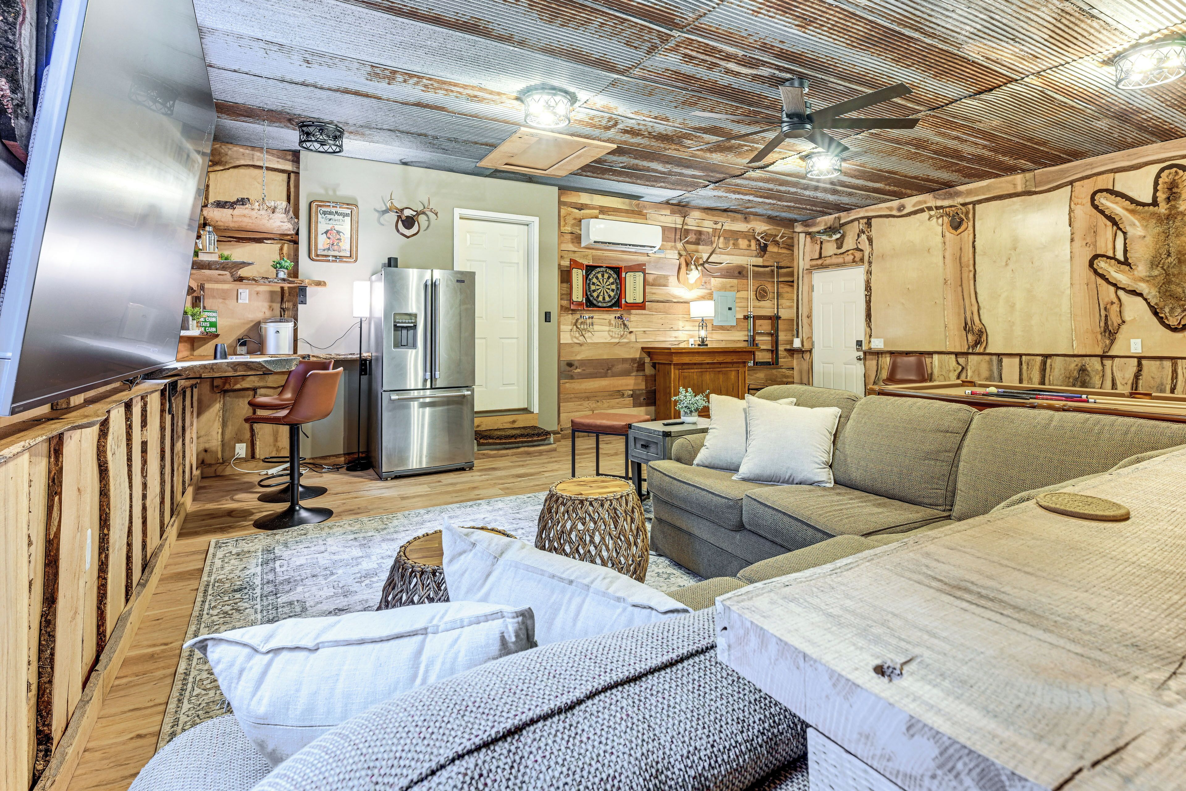 Un interior rústico con techo de madera, una zona de bar, un área de descanso con sofá y cojines, y un refrigerador.