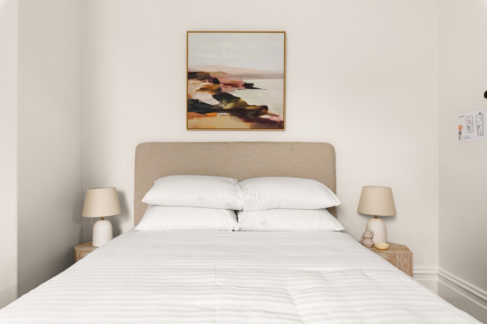 A neatly made bed with a striped bedspread, two bedside lamps, and a framed artwork on the wall.