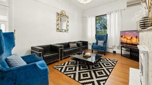 Ein modernes Wohnzimmer mit einem schwarzen Leder-Modulsofa, einem blauen Sessel, einem Glastisch und einem schwarz-weißen Teppich.