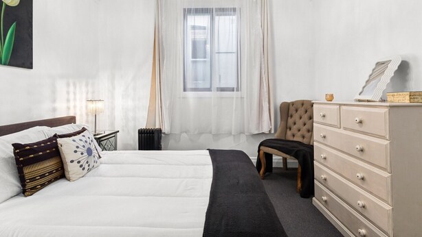 Ein Schlafzimmer mit einem Bett, einem Sessel, einem Schminktisch und einem Fenster mit Vorhängen.