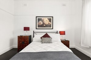 Ein ordentlich eingerichtetes Schlafzimmer mit einem Bett, zwei Nachttischen, einer Kommode und einem gerahmten Bild an der Wand.