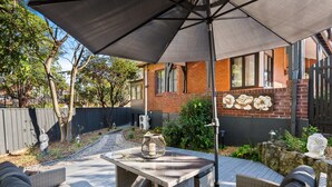 Eine Terrasse im Freien mit Tisch und Stühlen, einem großen Sonnenschirm und einer Wand mit floralen Dekorationen.