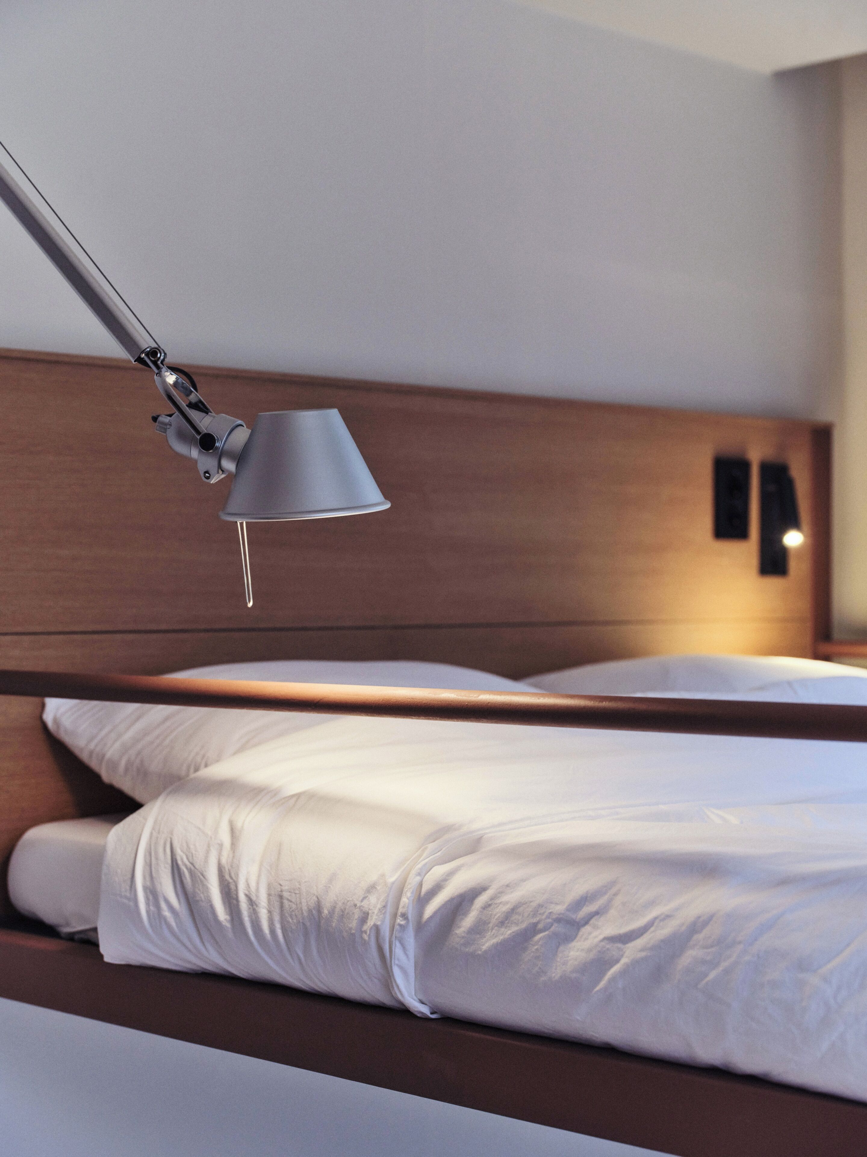 Un lit bien fait, avec du linge de lit blanc, une tête de lit moderne réglable et une seule lampe de chevet.