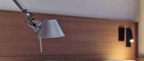 A neatly made bed with white linens, a modern adjustable headboard, and a single bedside lamp.