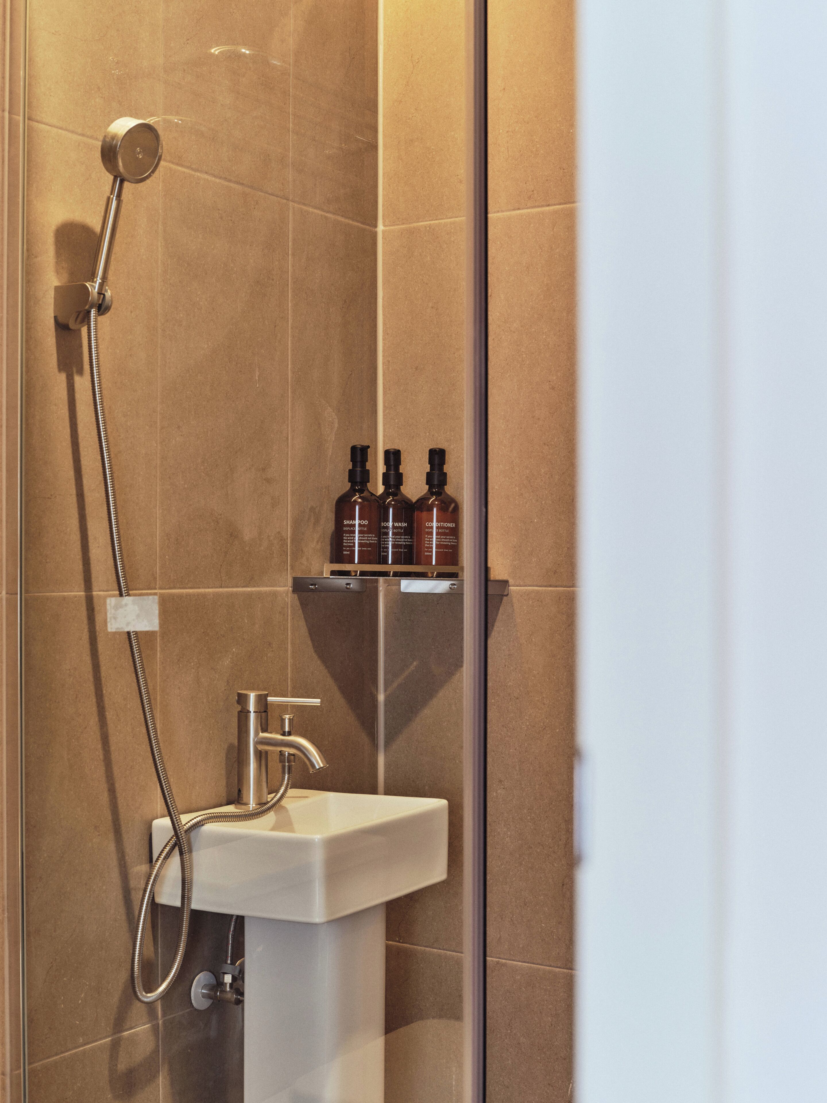 A bathroom with a shower, a sink, and a shelf with three bottles.