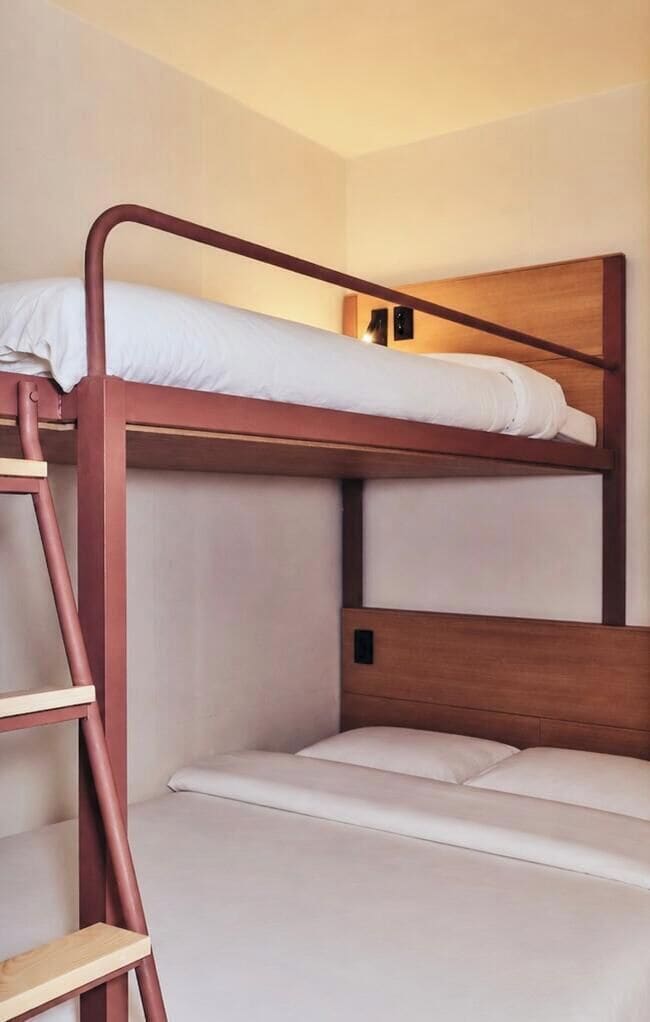Una cama litera con escalera, cabecera de madera y ropa de cama blanca.