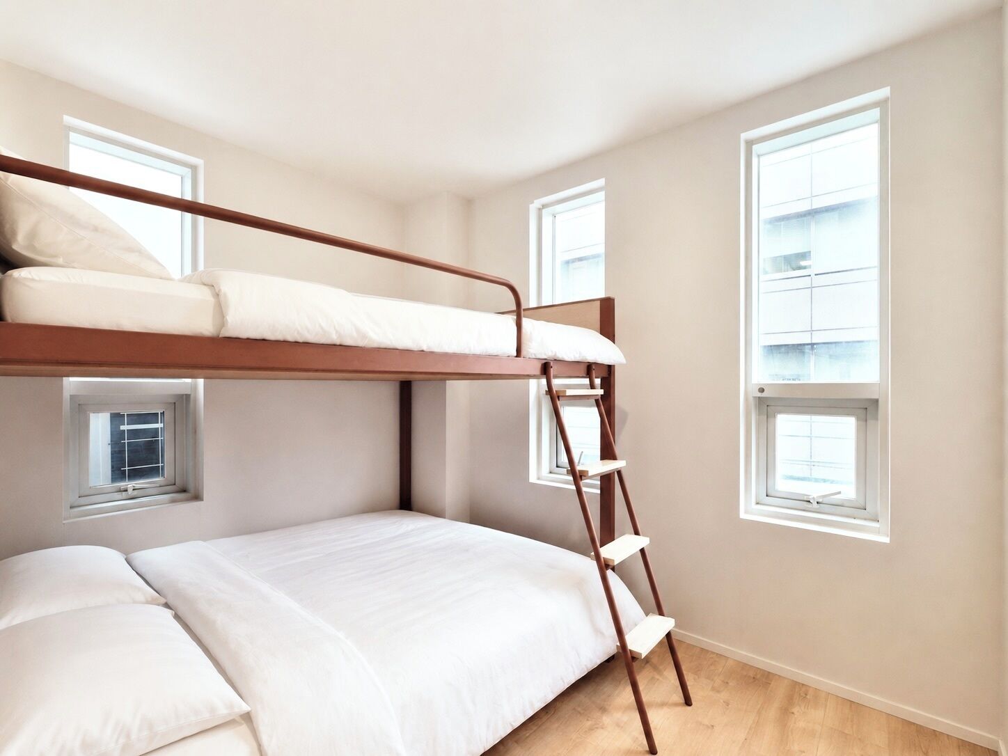 Habitación con literas, una escalera, dos ventanas y piso de madera.
