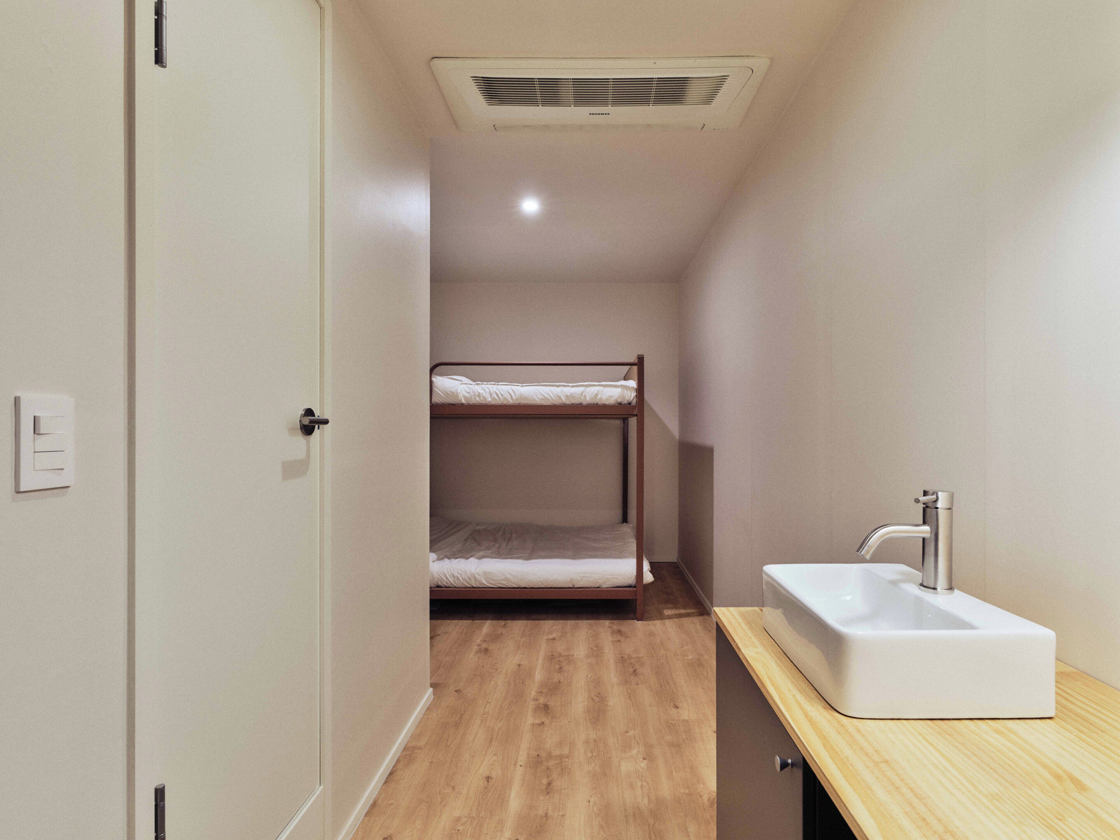 Habitación pequeña con una litera, un lavamanos y una puerta.