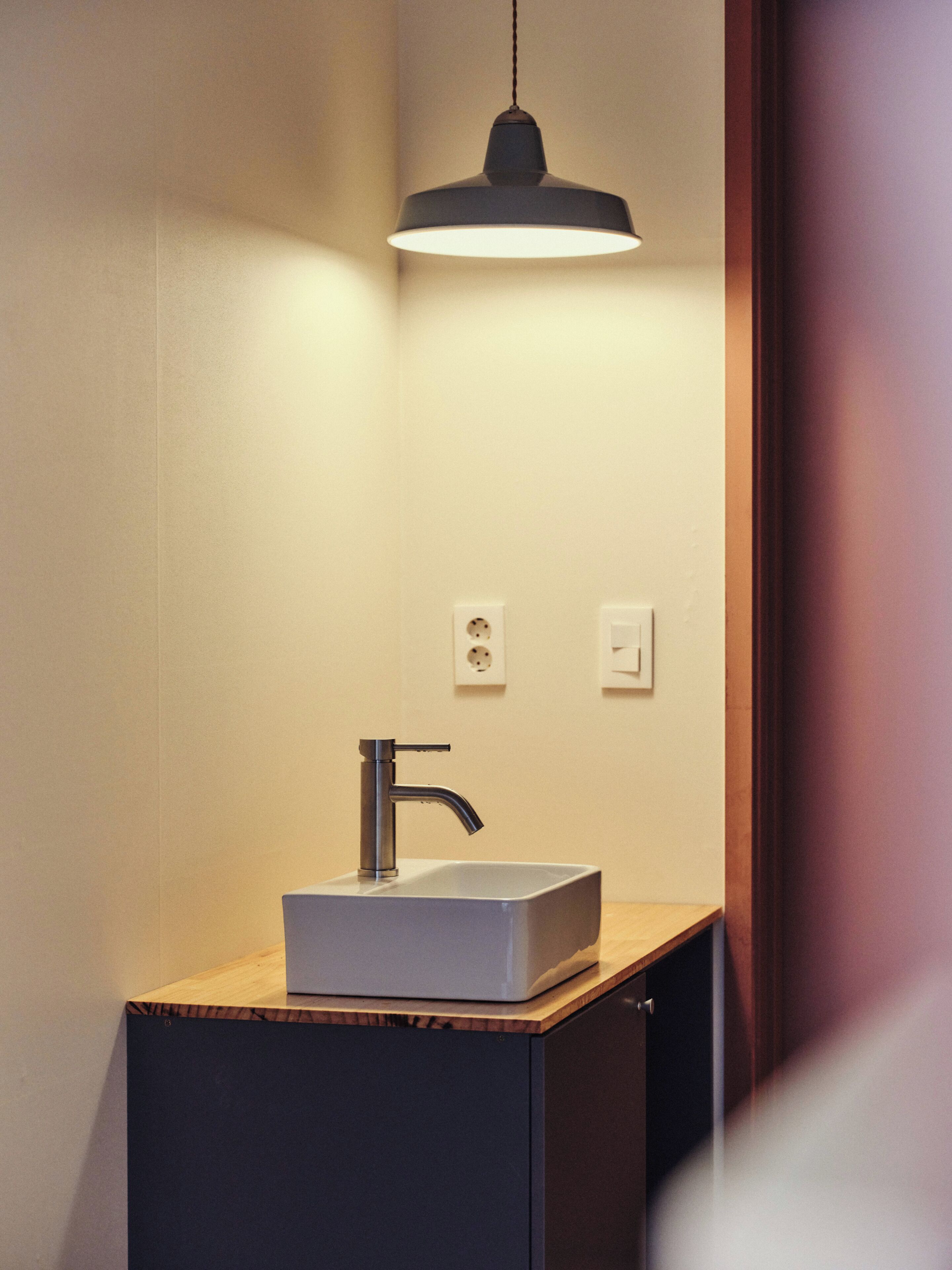 A modern bathroom with a rectangular sink, a single faucet, and a pendant light above.