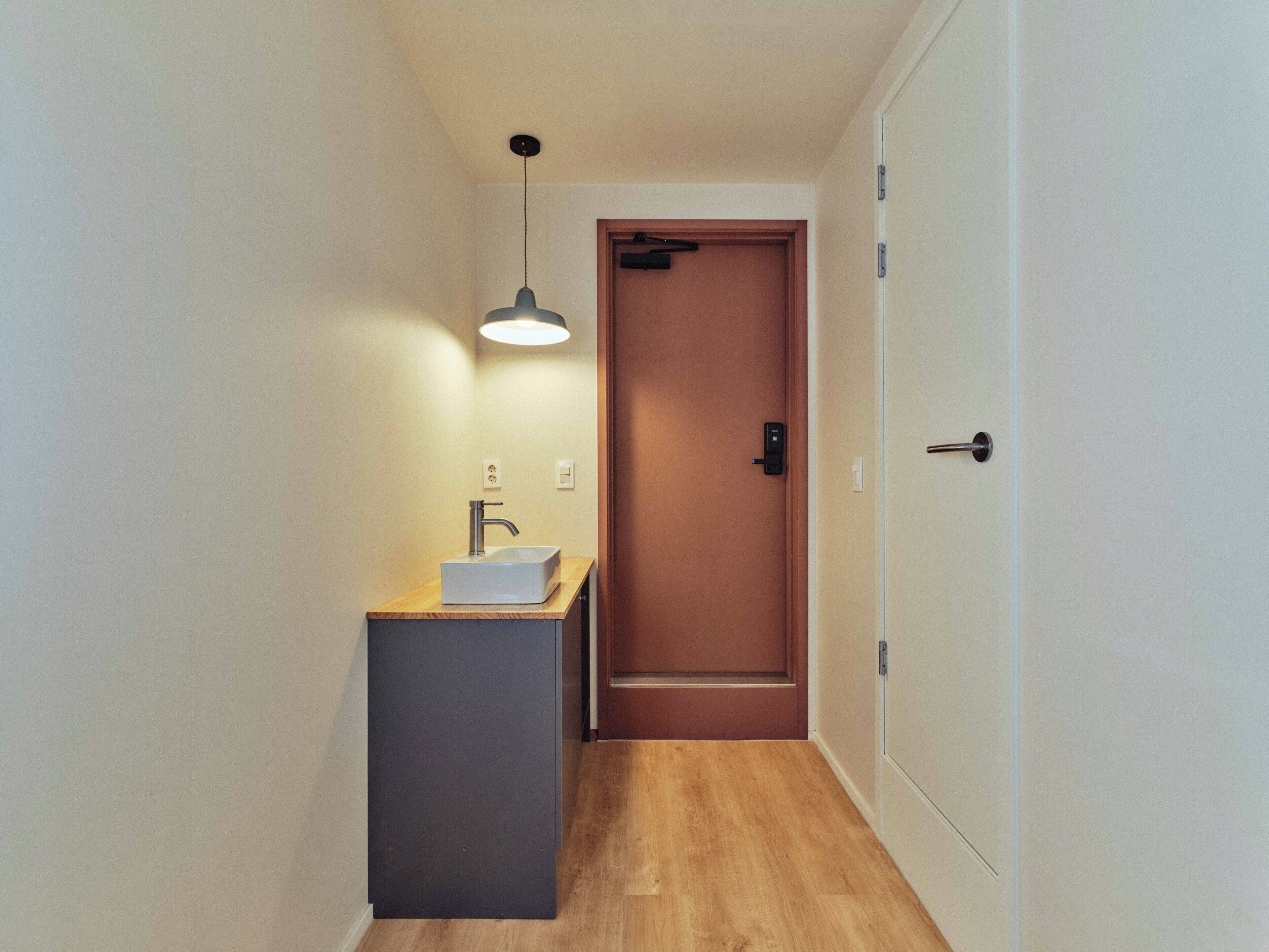 A narrow hallway with a wooden floor, a white door, and a small sink with a faucet.