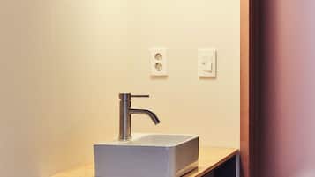Une salle de bain dotée d’un lavabo moderne, d’un luminaire suspendu et d’un plan de toilette en bois.