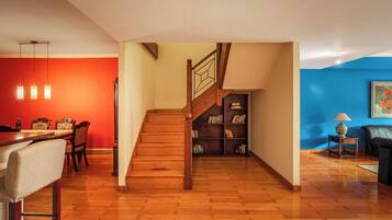 A modern living space with a wooden staircase, a dining area with a red wall, and a bookshelf.