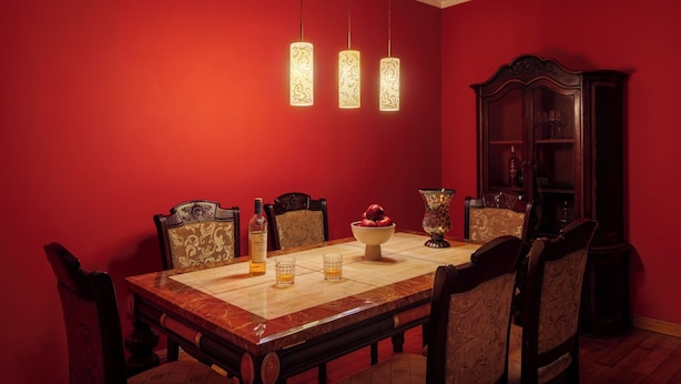 Comedor con pared roja, una mesa de madera y sillas. Hay tres lámparas colgantes sobre la mesa.