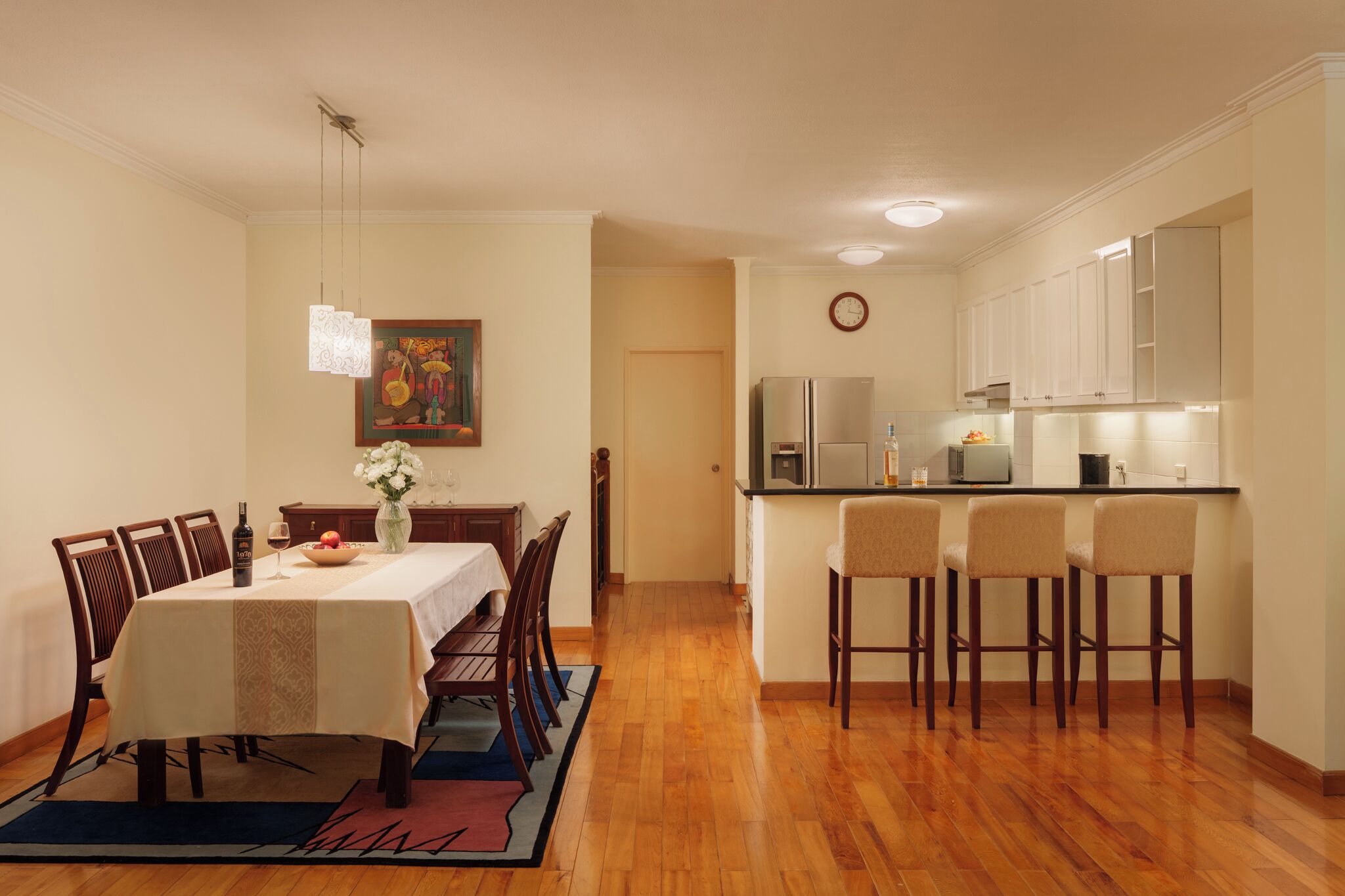 Uma sala de jantar com uma mesa posta para quatro pessoas, uma cozinha com eletrodomésticos modernos e um corredor que dá para outro quarto.