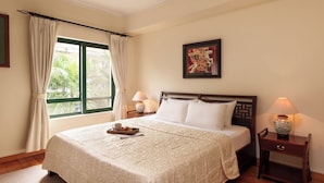 Habitación de hotel con una cama grande, dos mesitas de noche con lámparas, una ventana con cortinas y un cuadro en la pared.
