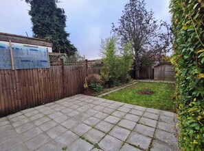Ein Garten mit einer gepflasterten Terrasse, einem Holzzaun und einem Schuppen.