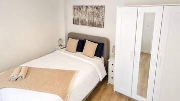 A bedroom with a bed, bedside table, lamp, wardrobe, and a hanging light fixture.