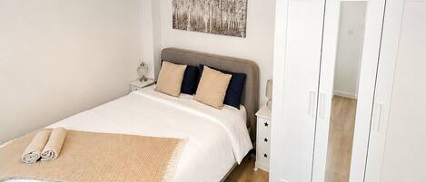A bedroom with a bed, bedside table, lamp, wardrobe, and a hanging light fixture.