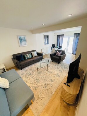 Ein modernes Wohnzimmer mit Sofa, Sesseln, Couchtisch und Fernseher.