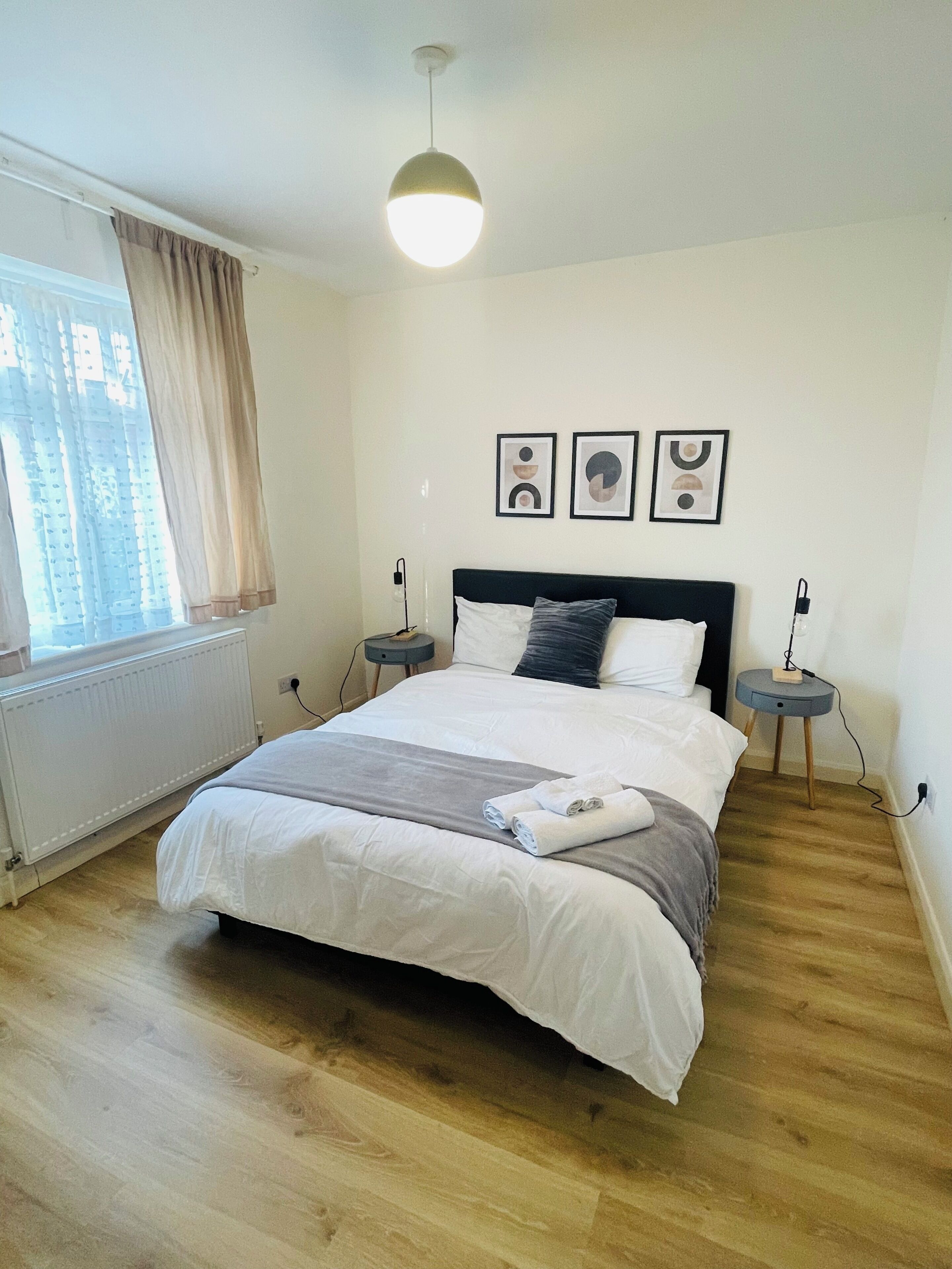 A bedroom with a bed, bedside tables, a window with curtains, and wall art.
