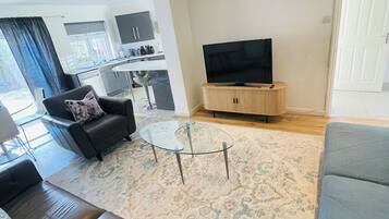 A living room with a sofa, a glass coffee table, and a television on a wooden stand.