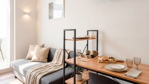 Un salon moderne avec un canapé, une table à manger agrémentée d’une plante et un téléviseur à écran plat fixé au mur.