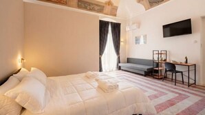 Une chambre d’hôtel avec un lit, un bureau, une chaise, une télévision et une fenêtre avec des rideaux.