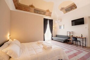Ein Hotelzimmer mit Bett, Schreibtisch, Stuhl, Fernseher und einem Fenster mit Vorhängen.