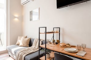 A modern living room with a sofa, a dining table with a plant, and a flat-screen TV mounted on the wall. - City Hub 6 | Historic Elegance & Modern Comfort in Bari (Bari)