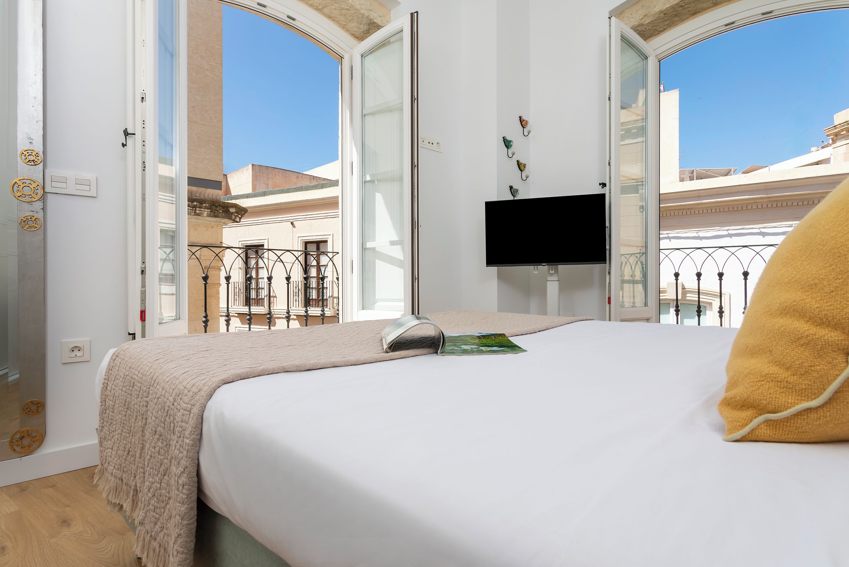 Habitación de hotel con cama, televisión en la pared y balcón con vista a la ciudad.